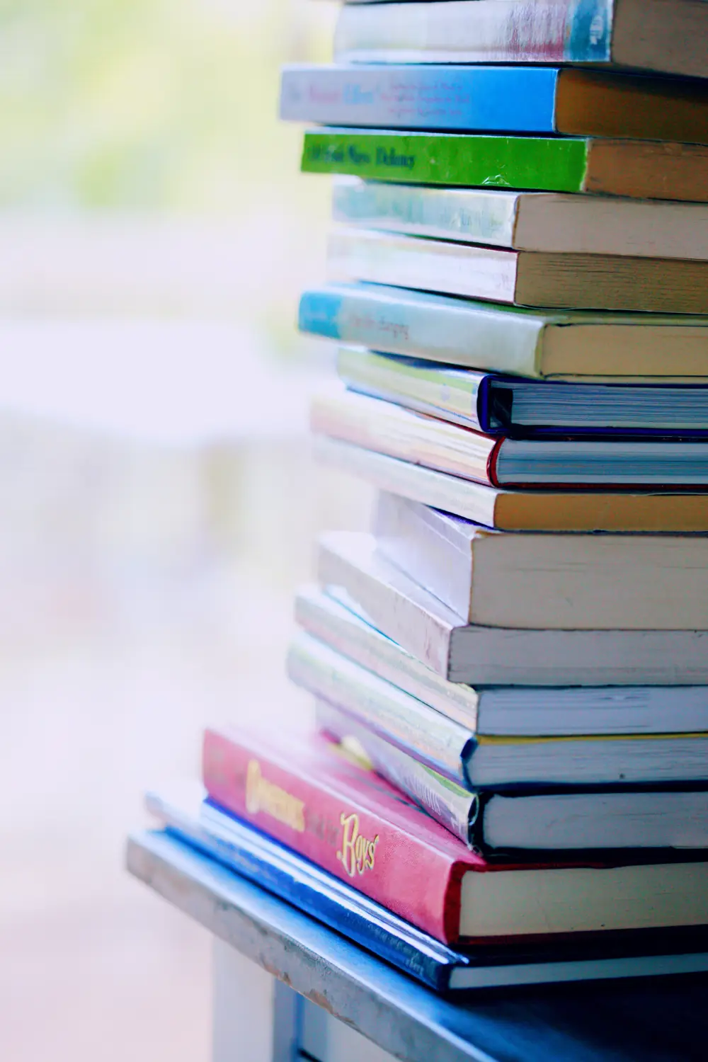 A tall stack of well-read books by a window